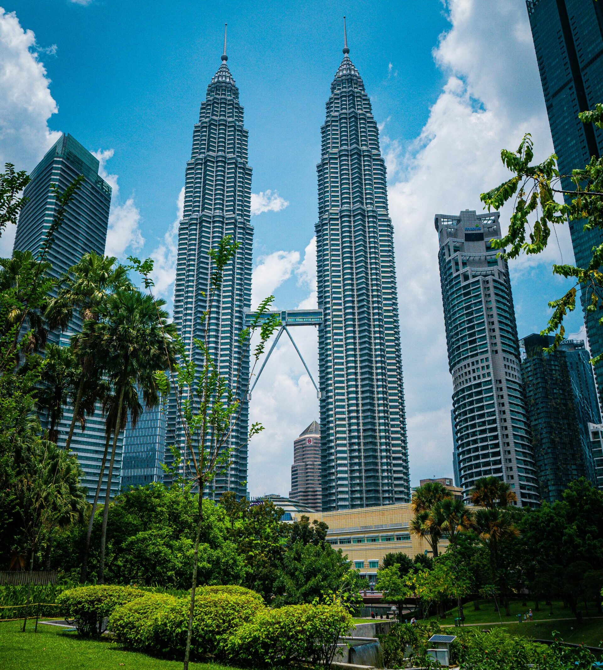 The iconic Petronas Twin Towers surrounded by greenery under a vibrant blue sky in Kuala Lumpur.