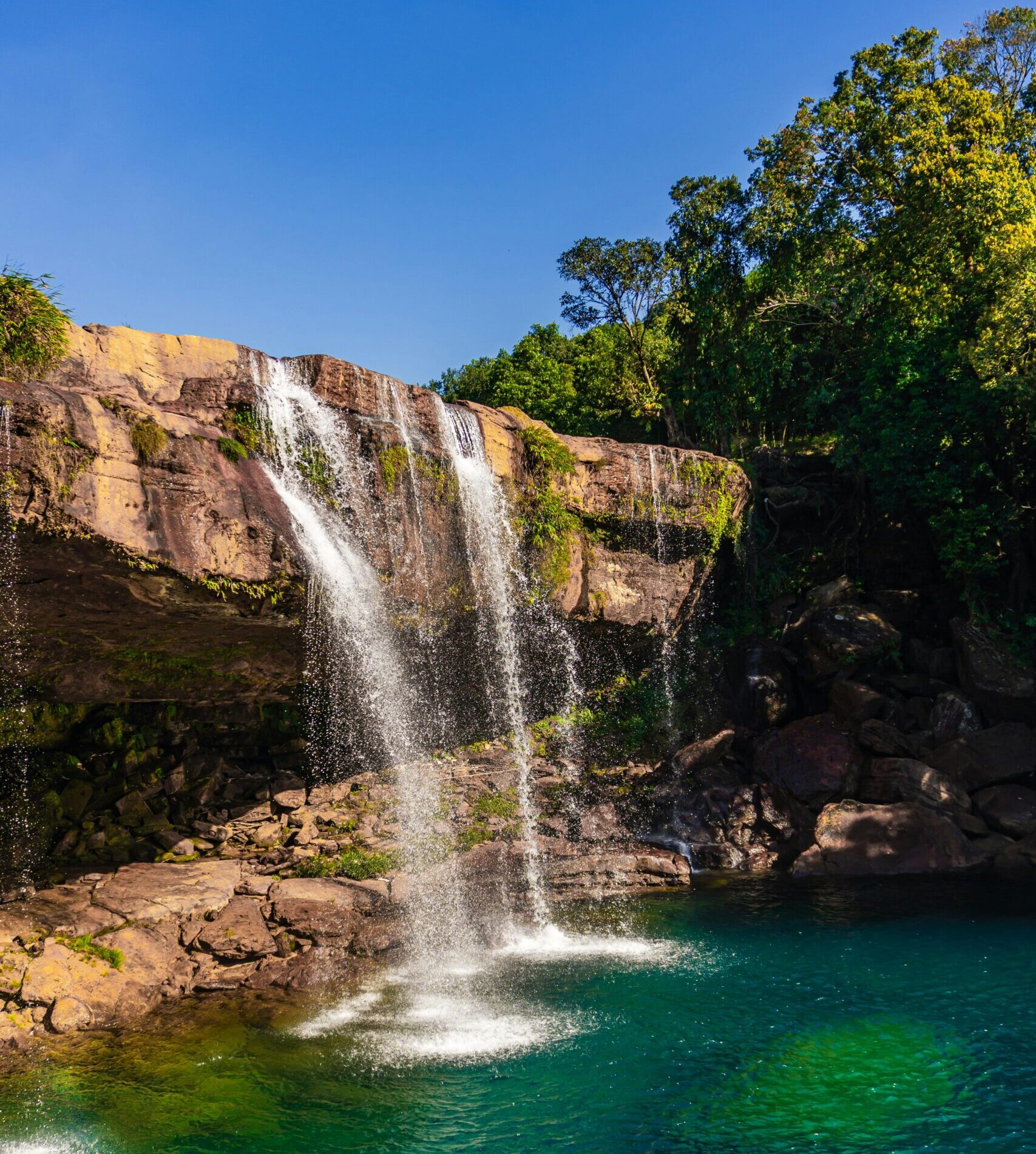 Scenic view of Krang Shuri Waterfall cascading into emerald waters in the lush Meghalaya forest.