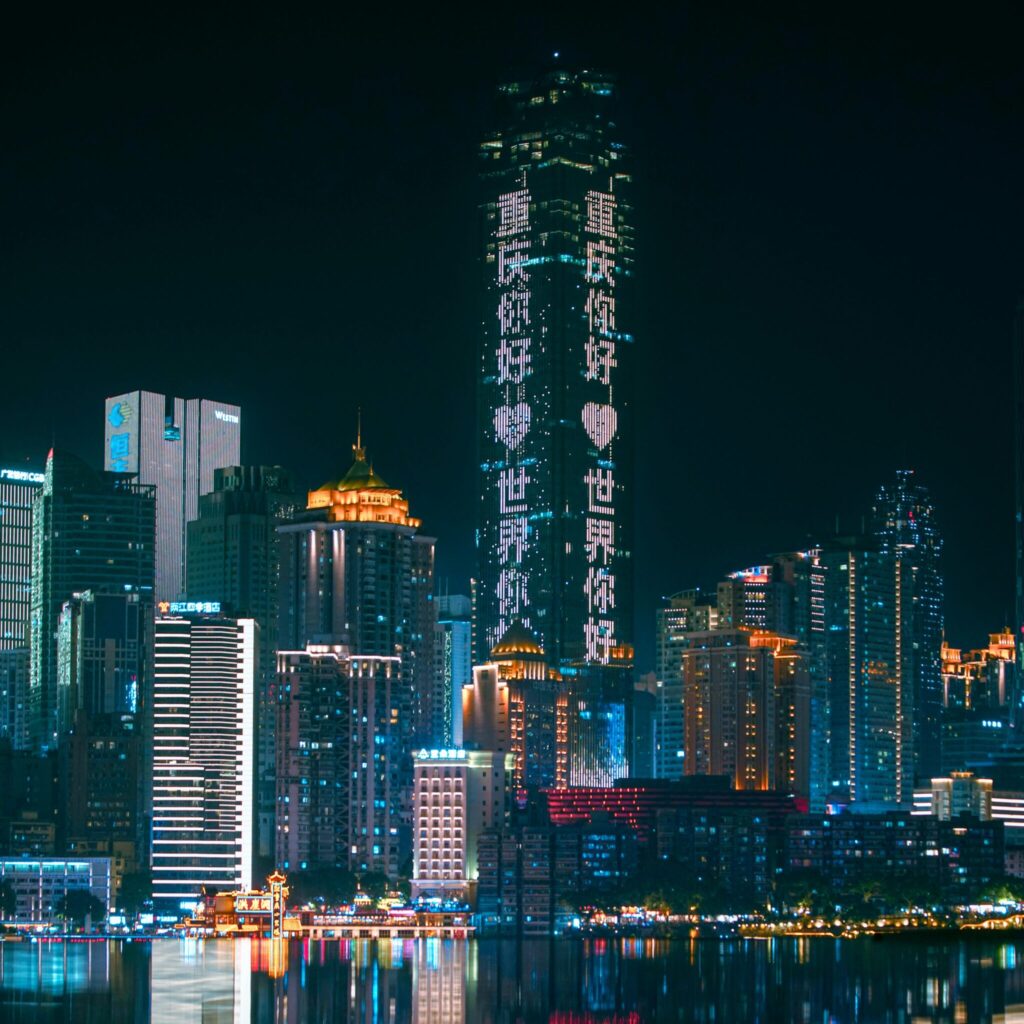 Chongqing skyline illuminated at night with neon lights reflecting on the river, showcasing urban futuristic architecture.